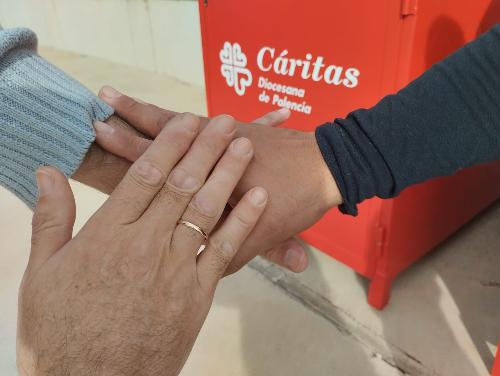 manos unidas sobre logo de C&aacute;ritas